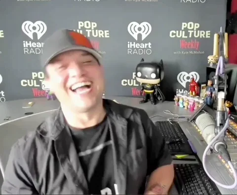 Guy at iHeartRadio Pop Culture Weekly studio laughing hard, genuine burst of laughter, cap and black shirt