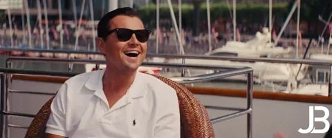 Leonardo DiCaprio on a yacht, sunglasses, white polo, laughing joyfully, luxury/success vibes, JB logo