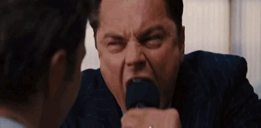 Leonardo DiCaprio screaming intensely into a microphone, close-up aggressive face, Wolf of Wall Street motivational speech scene