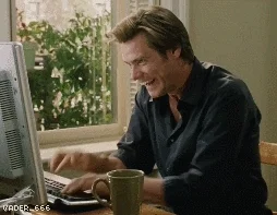 Jim Carrey in Bruce Almighty typing frantically on a computer and laughing maniacally, coffee mug beside him, VADER_666 watermark