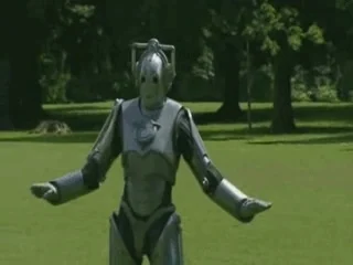 Cyberman (Doctor Who) dans un parc, bras écartés — robot, surprise, voilà