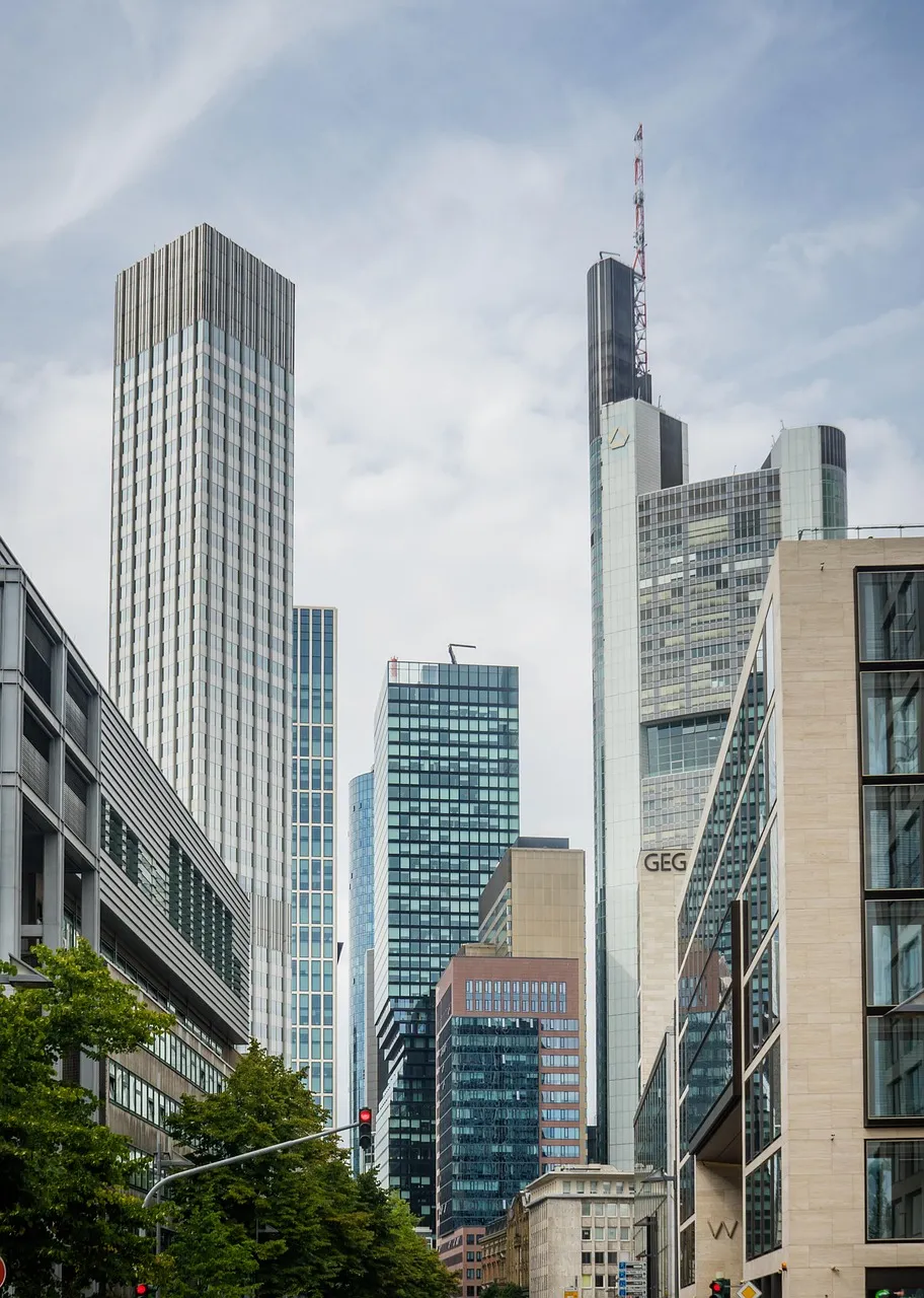 A cityscape with numerous modern skyscrapers under a cloudy sky, featuring a mix of architectural styles.