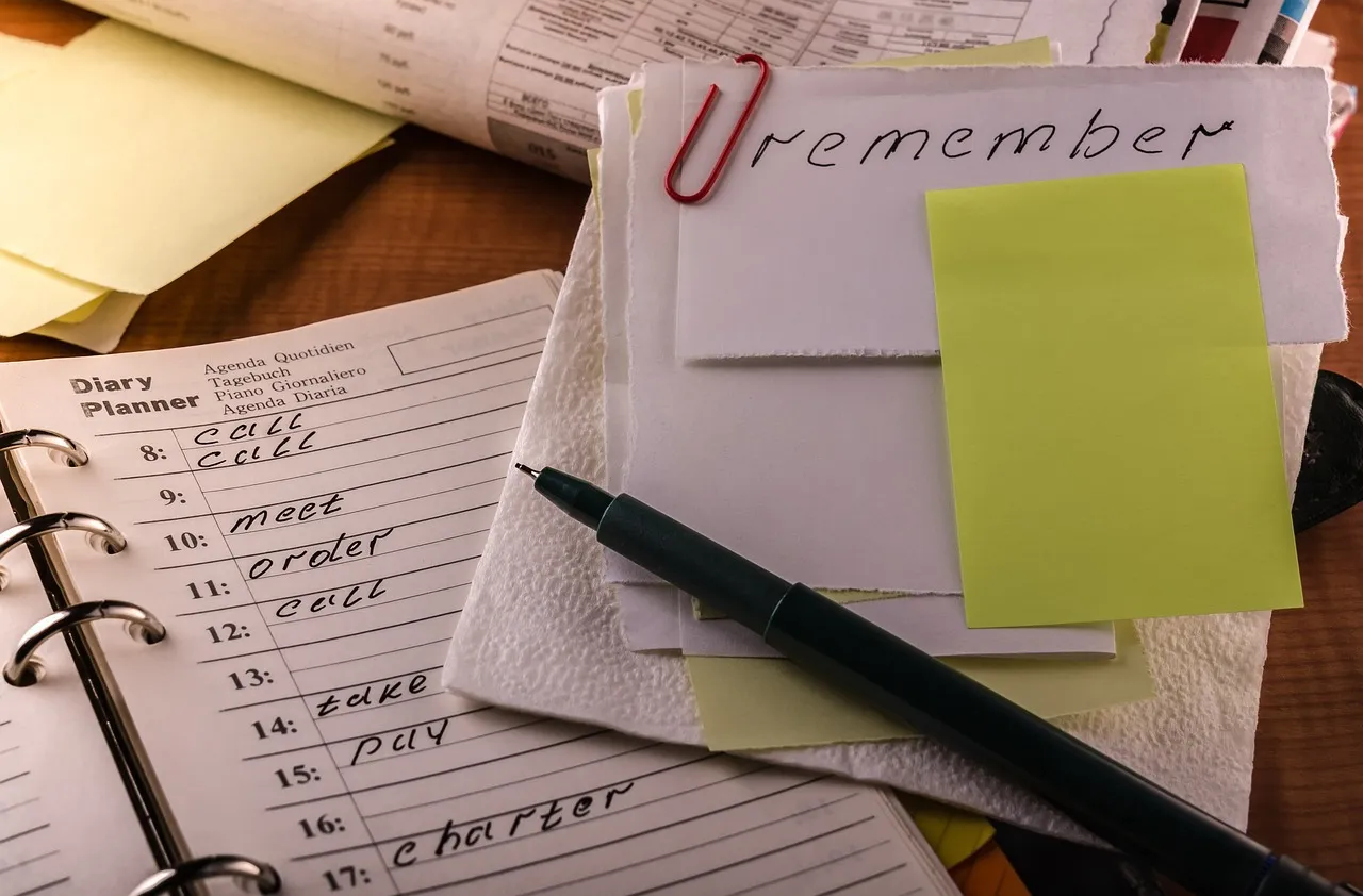 A diary planner, pen, and notes with "remember" written on one, suggesting tasks or reminders.