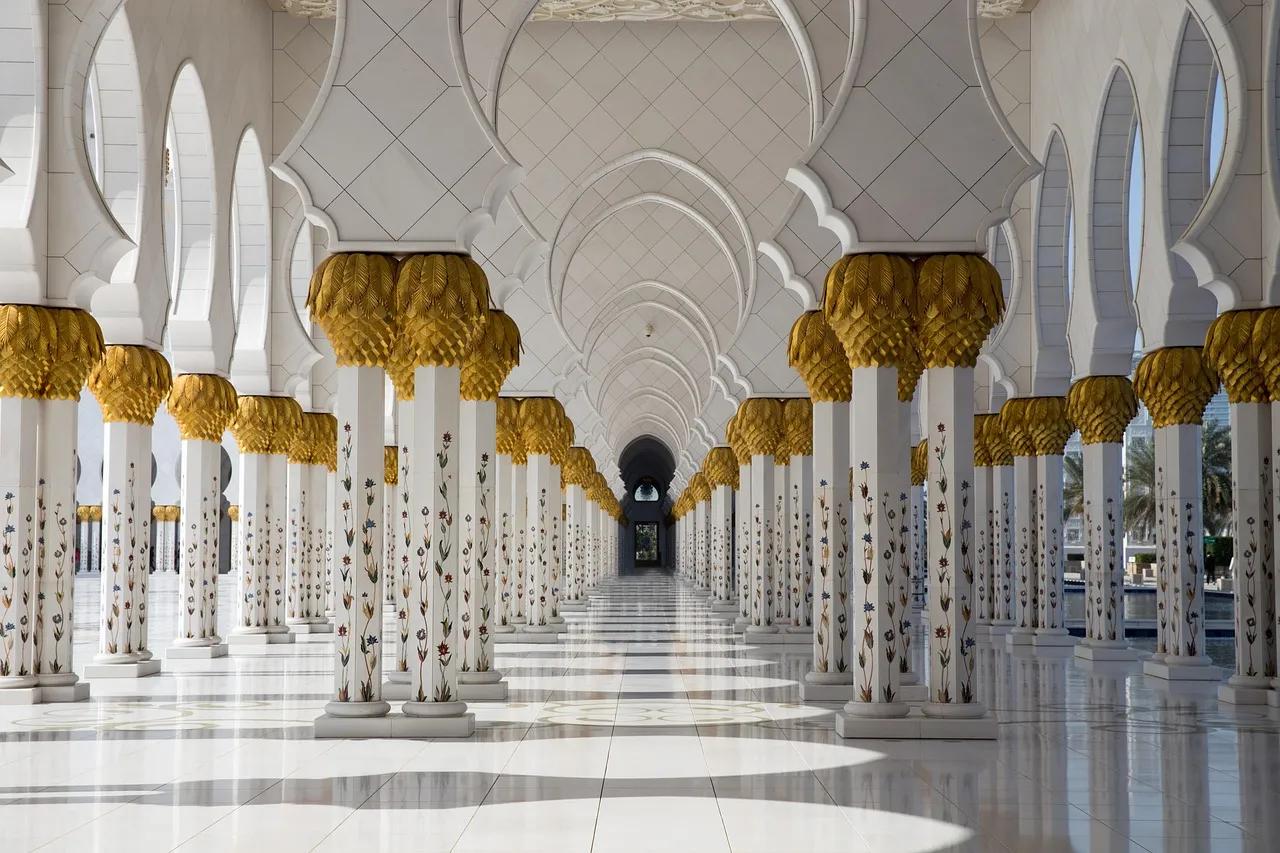 A grand, symmetrical hallway with ornate white pillars and golden capitals, leading to a distant archway.