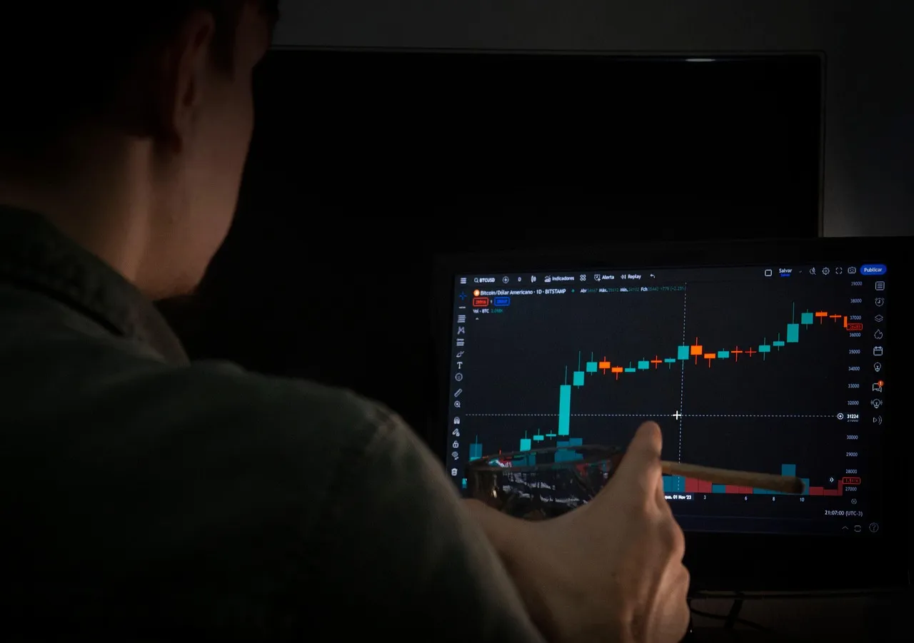 A person views a cryptocurrency trading chart on a screen in a dimly lit room.