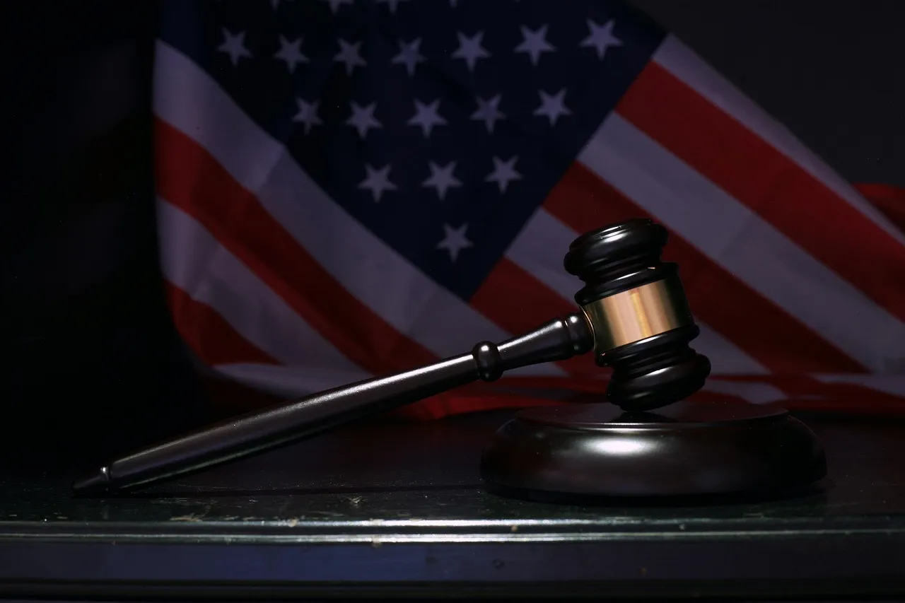 A gavel rests on a dark surface with a blurred American flag in the background.