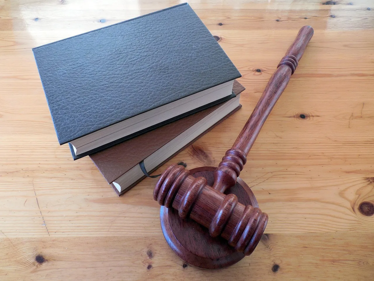 A wooden gavel and a stack of books on a light wooden table.