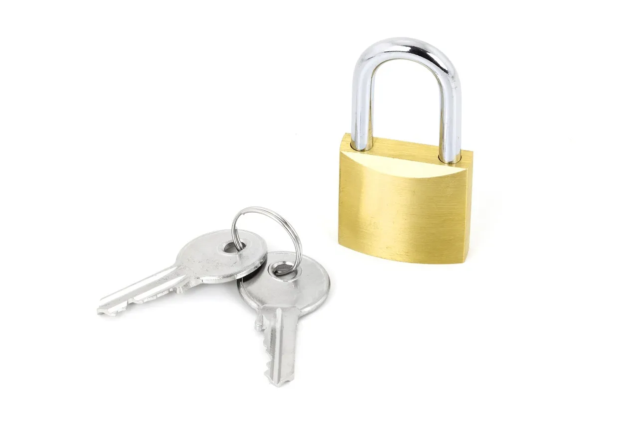 A brass padlock with a chrome shackle and two silver keys on a white background.