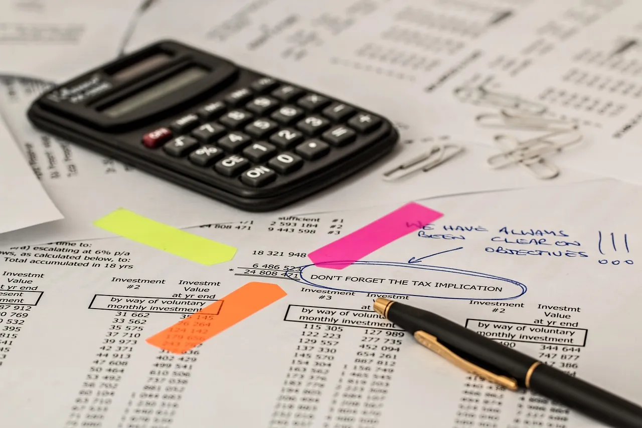 A calculator, pen, and financial documents with notes and highlights on a desk.