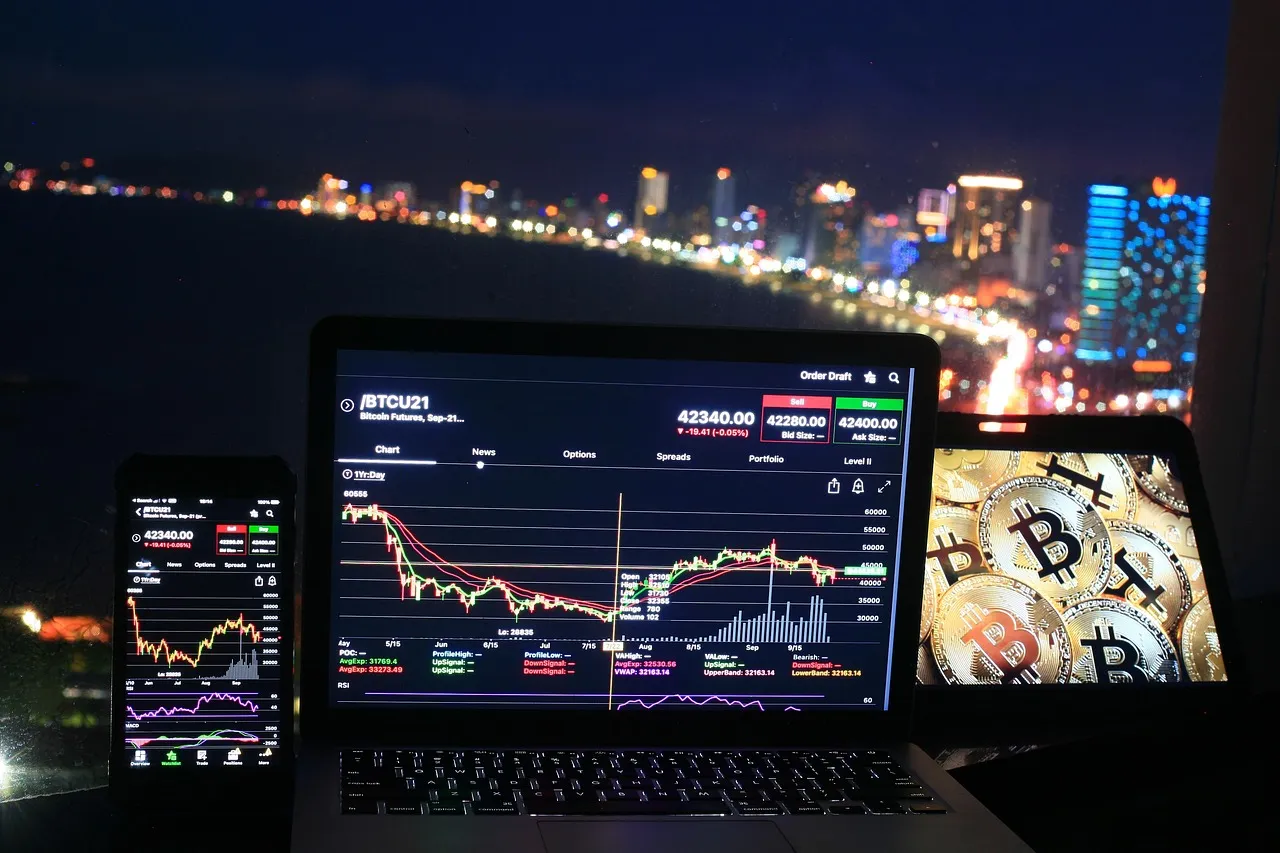 A laptop and smartphone display cryptocurrency charts with a city skyline at night.