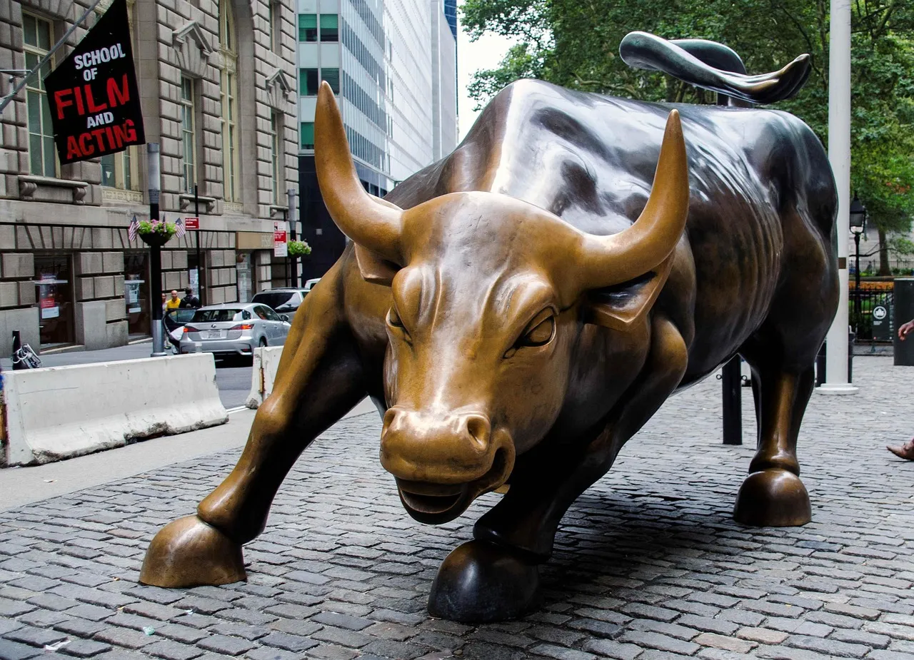 The Charging Bull statue on Wall Street, with a "School of Film and Acting" banner in the background.